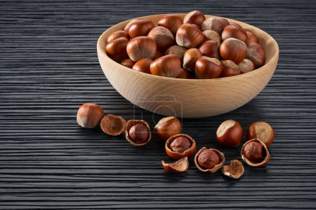 Foto de Wooden plate with organic hazelnut nuts on black table. - Imagen libre de derechos