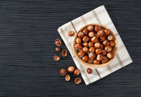 Photo for Wooden plate with hazelnut nuts on black table. Space for text - Royalty Free Image