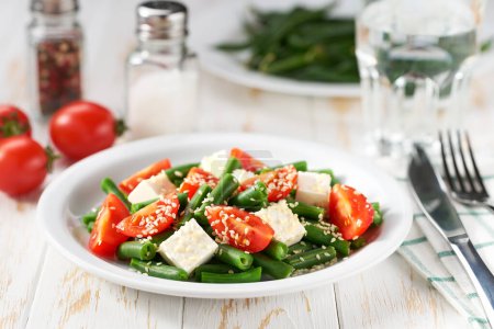 Foto de Judías verdes griegas y tomate, hierbas y aceite de oliva en un plato blanco servido con queso feta. - Imagen libre de derechos
