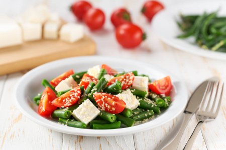 Foto de Ensalada de verduras vegetarianas frescas con tomates, semillas de feta y sésamo en una mesa de madera blanca, comida saludable. - Imagen libre de derechos