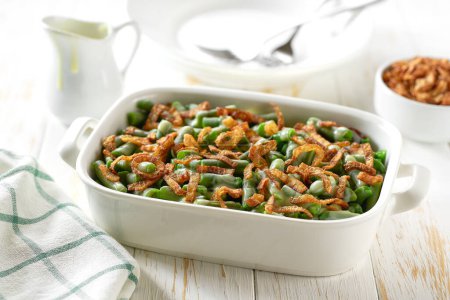 Téléchargez les photos : Casserole de haricots verts saupoudrée d'oignons frits croustillants servis sur un plat de cuisson en céramique. - en image libre de droit