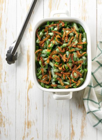 Photo for Green bean casserole sprinkled with crispy fried onions served on ceramic cooking baking dish, top view. - Royalty Free Image