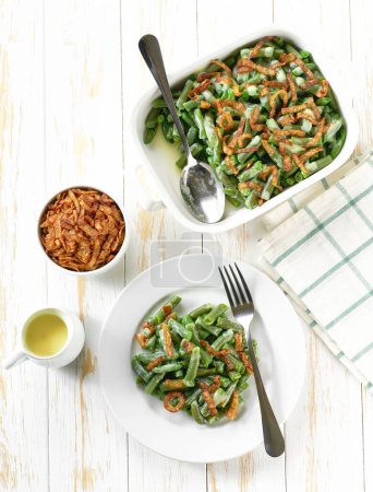 Photo for Delicious green bean casserole with crispy fried shallots onions on a white wooden table, top view.  Healthy summer veggie food. - Royalty Free Image