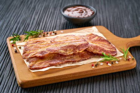 Téléchargez les photos : Rashers au bacon frit et sauce barbecue sur une table noire. lanières de bacon frit et sauce barbecue sur une table de cuisine noire. - en image libre de droit