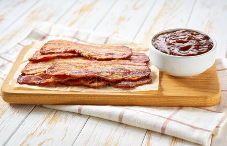 Photo for Fried bacon rashers and bbq sauce on a white wooden table. fried bacon strips and bbq sauce on a white kitchen table. - Royalty Free Image