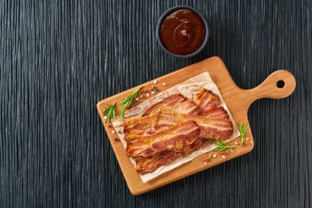Photo for Fried bacon rashers and bbq sauce on a black table, copy space for text.  fried bacon on black kitchen table top view. - Royalty Free Image