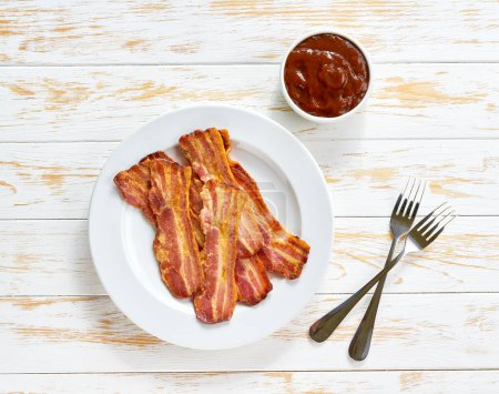 Photo for Fried bacon with bbq sauce in a dish on a white table, top view. - Royalty Free Image