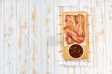 Photo for Fried bacon rashers and bbq sauce on a table, copy space for text.  fried bacon on white kitchen table top view. - Royalty Free Image