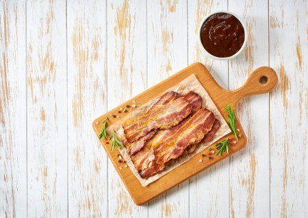 Photo for Fried bacon strips and bbq sauce on a table, top view. - Royalty Free Image