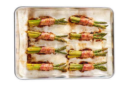 Photo for Roasted bundles of green asparagus wrapped in bacon on a baking tray isolated on a white background. - Royalty Free Image