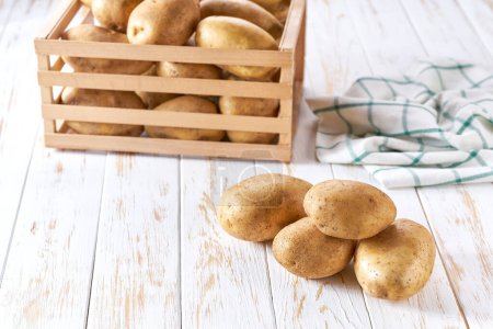 Téléchargez les photos : Pomme de terre biologique fraîche sur une table en bois avec une boîte à pommes de terre en arrière-plan. - en image libre de droit