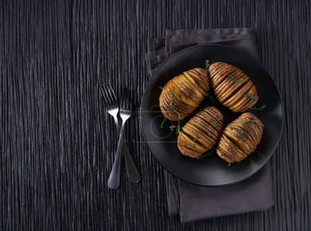 Photo for Baked hasselback potato with garlic, thyme and sea salt on a dark table. Crispy roasted Hasselback potato. - Royalty Free Image