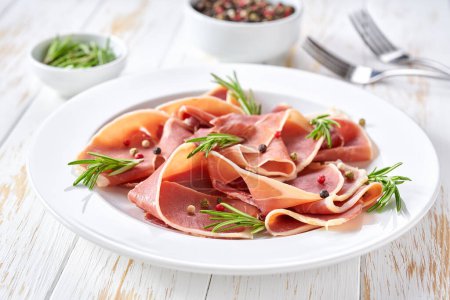 Photo for Parma ham prosciutto with rosemary and spices in a plate on a white wooden table . - Royalty Free Image
