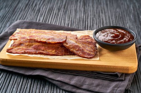 Photo for Fried bacon rashers and bbq sauce on a black table. fried bacon strips and bbq sauce on a black kitchen table. - Royalty Free Image