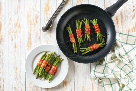 Téléchargez les photos : Haricots verts frits enveloppés dans du bacon et servis dans une poêle à frire sur une table en bois, vue sur le dessus. - en image libre de droit