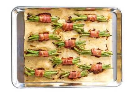 Téléchargez les photos : Faisceaux rôtis de haricots verts enveloppés dans du bacon sur une plaque de cuisson isolée sur un fond blanc. Vue du dessus. - en image libre de droit