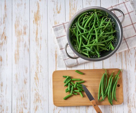 Téléchargez les photos : Haricots verts frais entiers et hachés sur une table de cuisine blanche, vue sur le dessus. - en image libre de droit