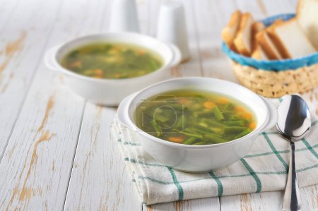 Téléchargez les photos : Deux bols de soupe de haricots verts avec des légumes sur une table de cuisine blanche. - en image libre de droit