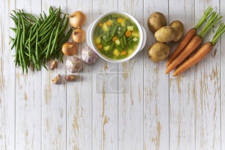 Foto de Sopa verde con papa, frijol verde y zanahoria en un plato blanco en la mesa de madera, vista superior. - Imagen libre de derechos