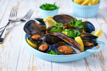 Photo for Freshly cooked mussels with lemon and parsley on a white table, selective focus. - Royalty Free Image