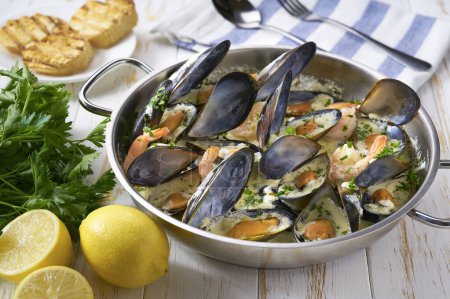 Photo for Mussels clams  in cream sauce in cooking pan and toasted bread on wooden table. - Royalty Free Image