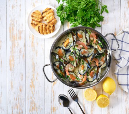 Photo for Mussels clams in cream sauce in cooking pan and toasted bread on wooden table. - Royalty Free Image