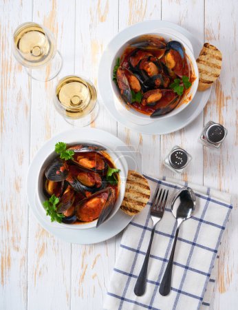 Photo for Mussels in tomato sauce, served with crispy bread. Tasty food with clams in a bowl, on white wood background. - Royalty Free Image
