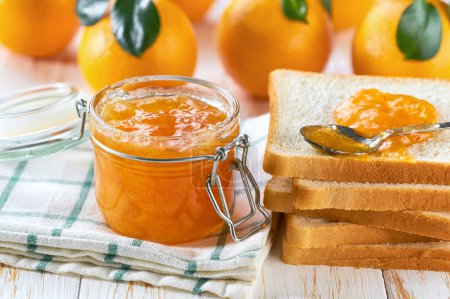 Photo for Jar of tasty orange jam on a white wooden table. Slices of oranges and green leaf on table. - Royalty Free Image