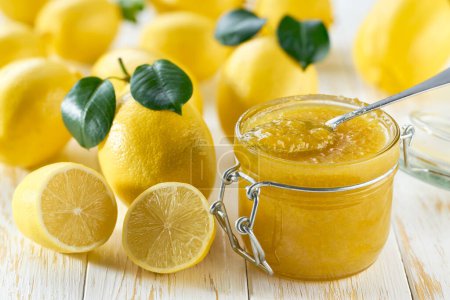 Photo for Close-up of glass jar with lemon jam on white table with lemon slices, selective focus. This jam can be used for spreading white bread, filling cakes, etc - Royalty Free Image