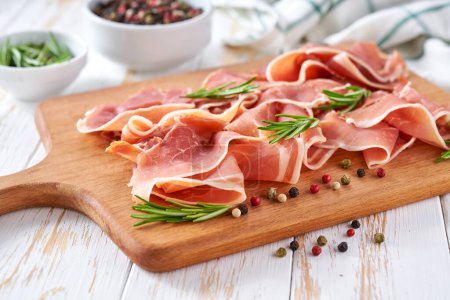 Photo for Italian parma ham prosciutto with rosemary and pepper on a white wooden table, selective focus. - Royalty Free Image