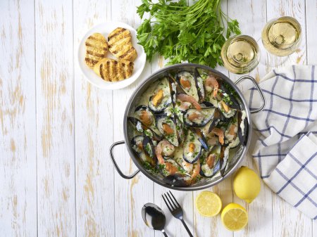 Photo for Mussels clams in cream sauce in cooking pan and toasted baguet on wooden table, top view. - Royalty Free Image