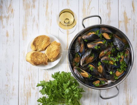 Photo for Mussels with white wine in cooking pan.Boiled mussels with parsley and white wine on wooden table, top view. - Royalty Free Image