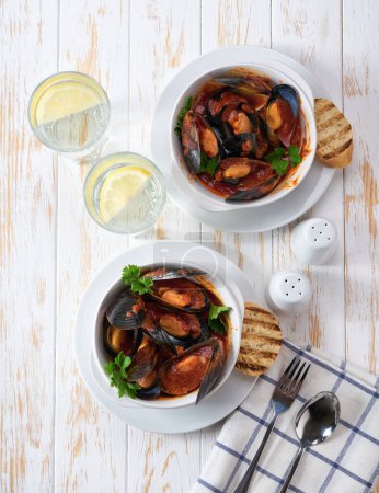Photo for Two bowls with mussels soup with tomato sauce and toasted baguette on a white table, top view. - Royalty Free Image