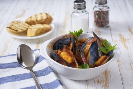 Photo for Traditional tomato soup with mussels with and toasted baguette on a white table. - Royalty Free Image