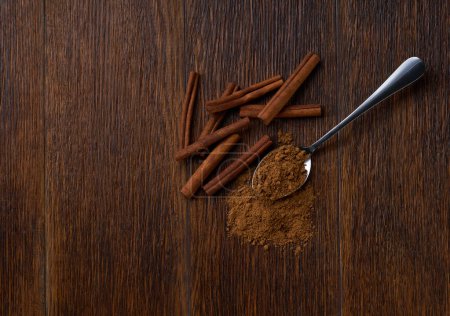 Photo for Cinnamon powder in a metal spoon on a brown wooden table, top view. - Royalty Free Image