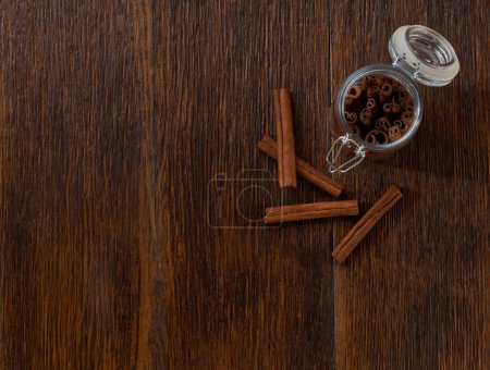Photo for Cinnamon sticks in a storage jar on a brown wooden table, top view. - Royalty Free Image