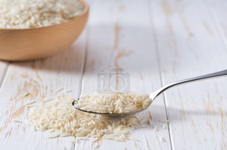 Photo for Metal spoon with long rice basmati on a white wooden table. - Royalty Free Image