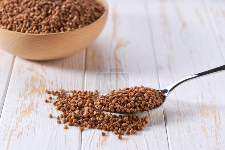 Photo for Metal spoon with raw buckwheat on a light table, selective focus. - Royalty Free Image