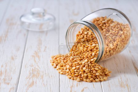 Photo for Dry yellow peas spill out of a glass storage jar on a light table, selective focus. - Royalty Free Image