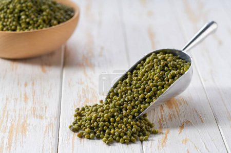 Photo for Green mung beans spill out of a metal scoop on a light table, selective focus. - Royalty Free Image
