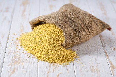 Photo for Organic millet yellow grains in sack bag. Sack with organic grains of millet . Organic grains of millet in burlap bag and heap of grains of millet. - Royalty Free Image
