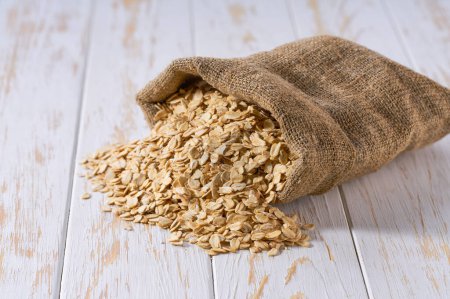 Photo for Dry rolled oats in sack bag. Sack with oatmeal flakes . Organic oatmeal flakes in burlap bag and heap of dry rolled oats. - Royalty Free Image