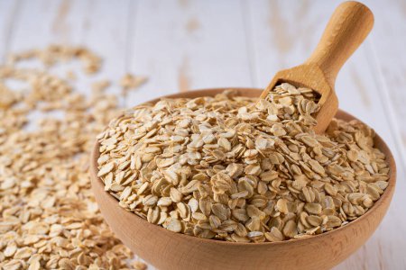 Photo for Organic dry rolled oats are scattered out of the wooden bowl on a light table, selective focus. - Royalty Free Image