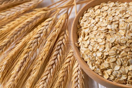 Photo for Raw dry rolled oats are scattered out of the wooden bowl on a light table, selective focus. - Royalty Free Image
