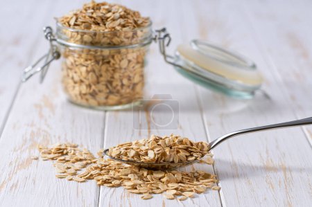 Photo for Metal spoon with organic dry rolled oats on a white wooden table. - Royalty Free Image