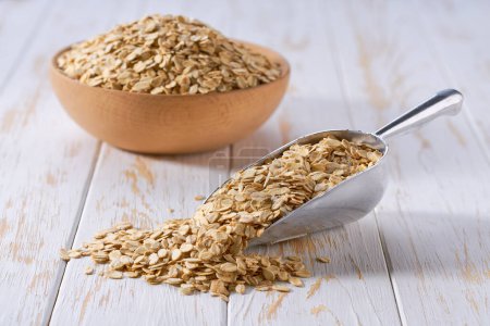 Photo for Organic dry rolled oats spill out of a metal scoop on a light table, selective focus. - Royalty Free Image