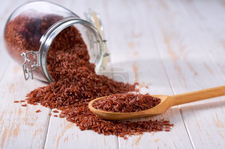Photo for Organic red rice in wooden scoop and in glass storage jar on a light table, selective focus - Royalty Free Image