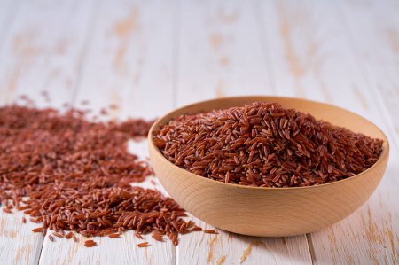 Photo for Raw red rice are scattered out of the wooden bowl on a light table, selective focus. - Royalty Free Image