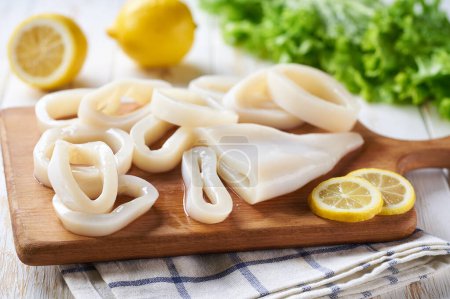 Photo for Sliced rings raw squid on white wooden table with lemon and herbs.  Fresh seafood concept. - Royalty Free Image