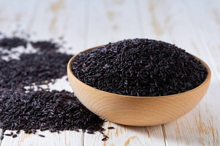 Photo for Organic grains of black rice are scattered in a wooden bowl close up. - Royalty Free Image